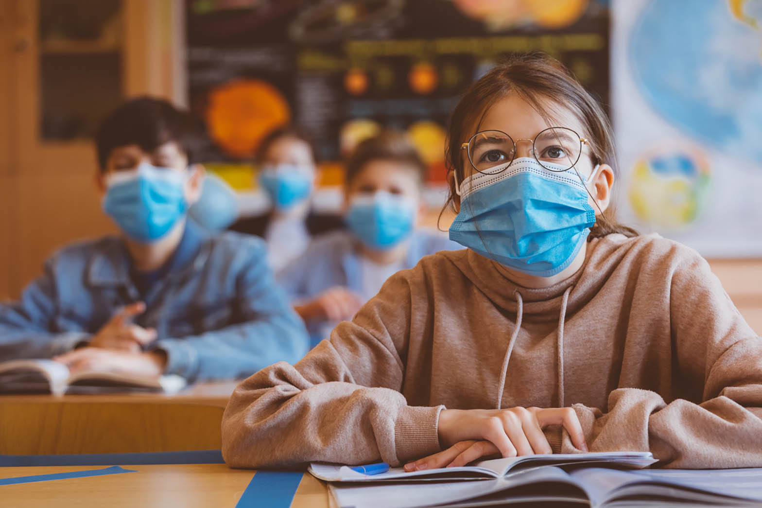 Mädchen mit Mund-Nasen-Schutz sitzt im Unterricht im Klassenzimmer