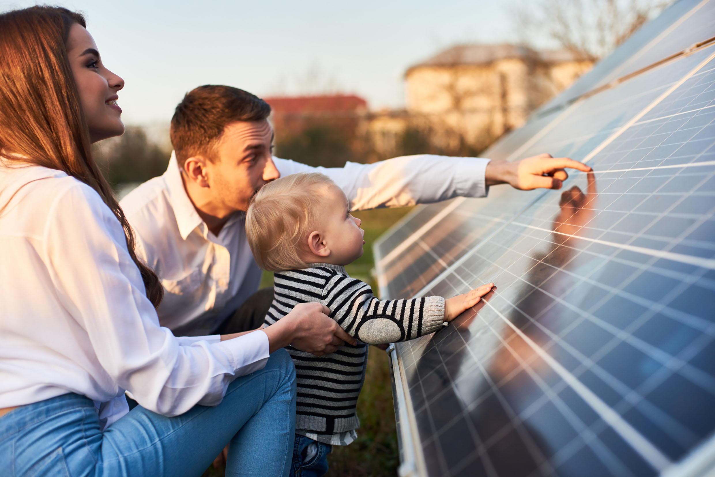 Seitliche Nahaufnahmeaufnahme einer jungen modernen Familie mit einem kleinen Sohn, der Solarpanel an einem sonnigen Tag kennenlernt, grünes alternatives Energiekonzept