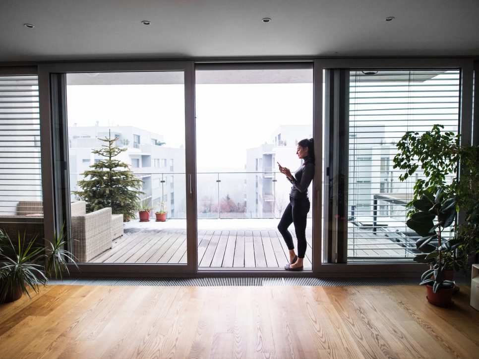 A woman with smartphone standing in an open door, text messaging.