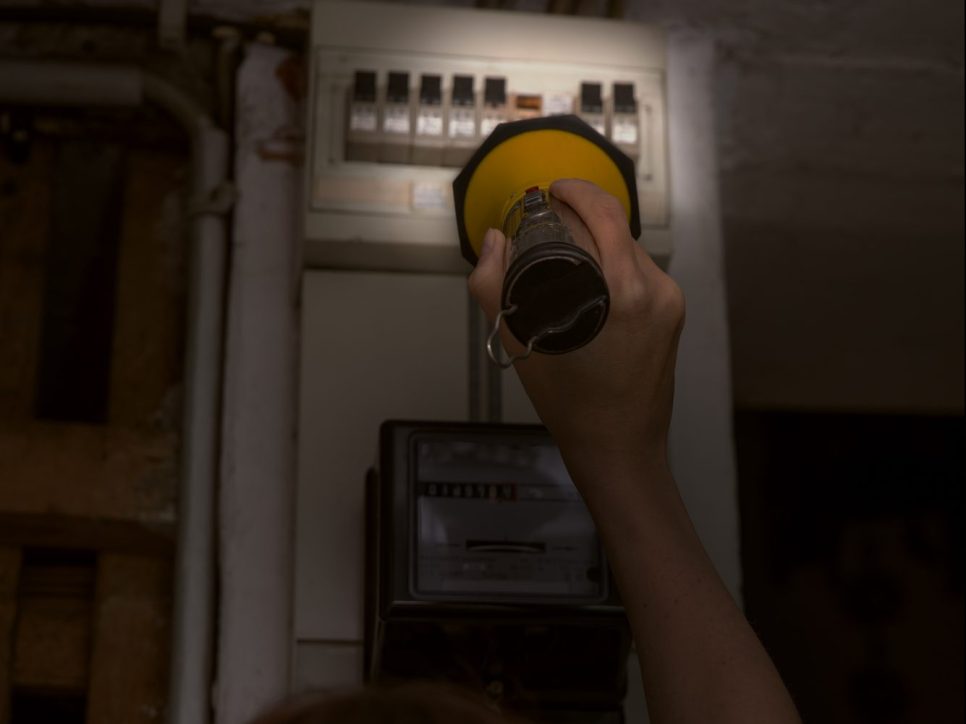 Blackout, electricity cut, woman with flashlight checking the breaker box, fuse box