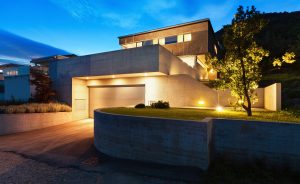 Modernes Wohnhaus mit Beton- und Glasarchitektur, beleuchtet bei Dämmerung, mit Garage, Auffahrt und gepflegtem Vorgarten.